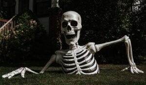 A skeleton sitting on the grass in front of a house